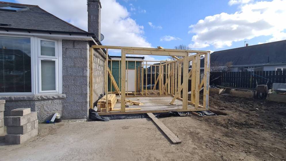 Timber frame extension structure rising against the original granite wall of an Aberdeen home