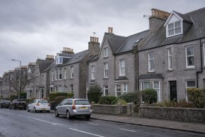 A terrace of granite houses with slate roofs and chimney stacks on an Aberdeen residential street under grey winter sky